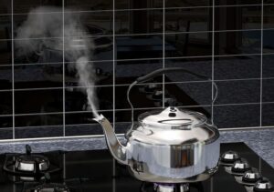 چاینک بالای اجاق گاز که آب آن جوش کرده است و به بخار تبدیل شده است